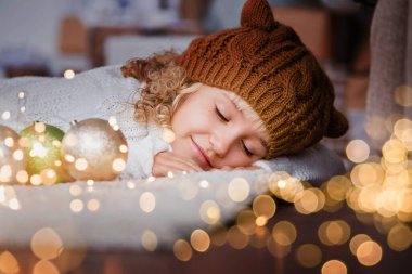 Noel ağacının yanında örülmüş şapkalı bir kız yeni yıl dileği diliyor. Noel arifesinde heyecanlı küçük kız. Umut Noel Baba 'yı bekliyor. Umutlu çocuk. Yeni yıl arifesi. Hayaller gerçek olur..