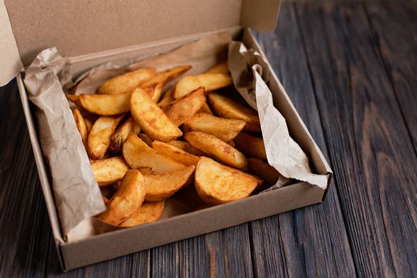 Slices of fried potatoes in box for food delivery. Delivered take away fast food on wooden background. Tasty fried potatoes from take away menu. Eco packaging. copy space. food delivery service