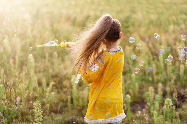 オレンジのドレスを着た女の子が畑で遊んでシャボン玉を吹いてた 村の自然 幸せな子供時代のコンセプト — ストック写真