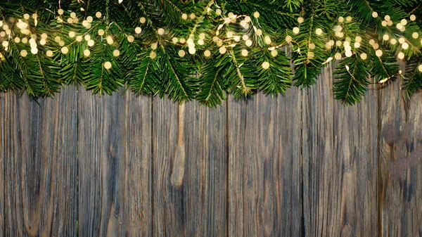 Christmas background with fir tree and light bokeh on dark wooden board. Copy space. Christmas or New Year Border. Xmas backdrop for your greeting card