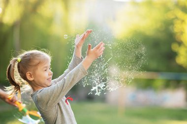 Happy 5 year old child bursts soap bubbles in garden. Summer vacation in nature. Emotional portrait of happy and active little beautiful girl bursting with soap bubbles laughing clipart