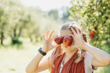 Sonbaharda çiftlikte elma toplayan bir çocuk. Ağaç bahçesinde oynayan küçük kız. Sağlıklı beslenme. Tatlı küçük kız kırmızı lezzetli meyve yiyor. Hasat Konsepti. Elma toplama.