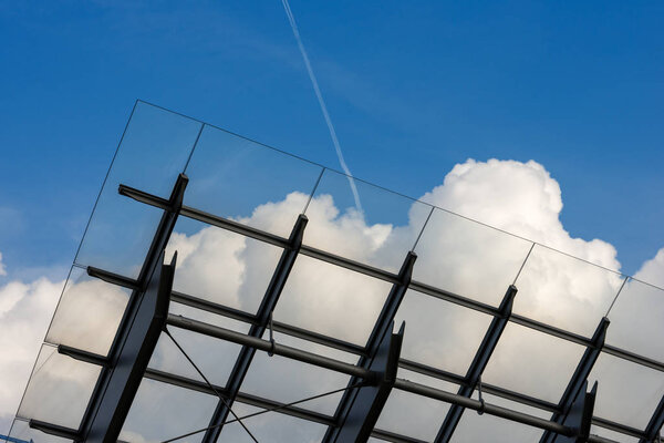 Detail of steel and glass roof of a modern building with blue sky and clouds