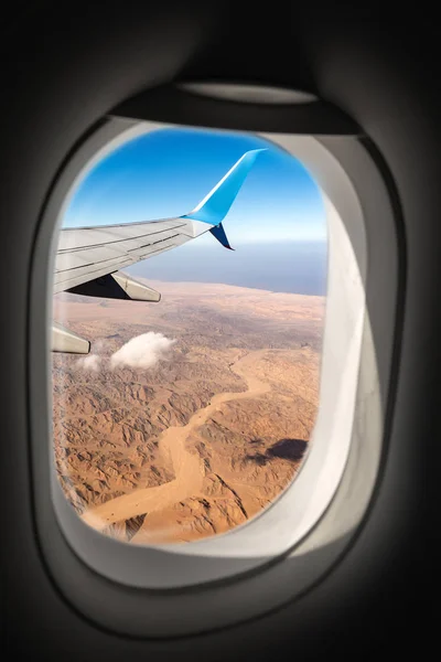 Aerial view of the Sahara Desert and Red Sea and the wing of a commercial airplane photographed through the porthole window.