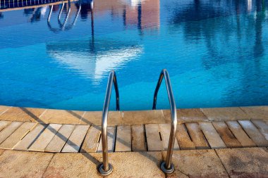 Paslanmaz çelik merdiven ile bir swimming pool ve bir plaj şemsiyesi yansıması ile mavi su yakın çekim 