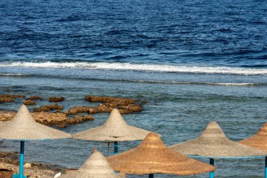 Marsa Alam, Mısır, Afrika yakınlarında Kızıldeniz. Resif üzerinde kırma dalgalar, ön planda bir grup saman plaj şemsiye 