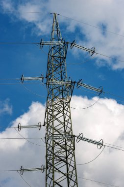 High voltage tower (power line) with electric cables and insulators, on a blue sky with clouds