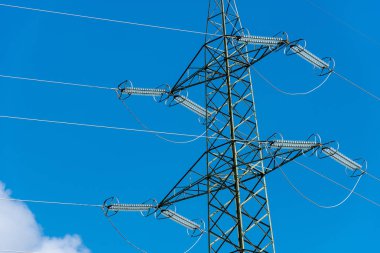 High voltage tower (power line) with electric cables and insulators, on a blue sky with clouds