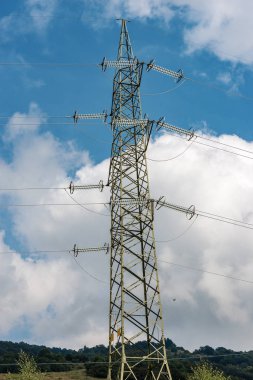 High voltage tower (power line) with electric cables and insulators, on a blue sky with clouds
