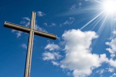 Wooden Christian cross on blue sky with clouds and sun rays - Religious Symbol clipart