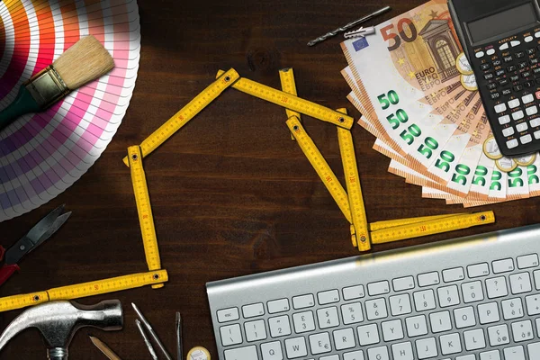 Home improvement concept - Wooden folding ruler in the shape of a house with work tools, calculator, banknotes and coins on a wooden des