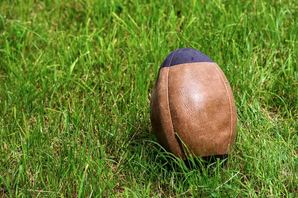 Stará hnědá a černá ragbyová koule na zelené trávě — Stock fotografie