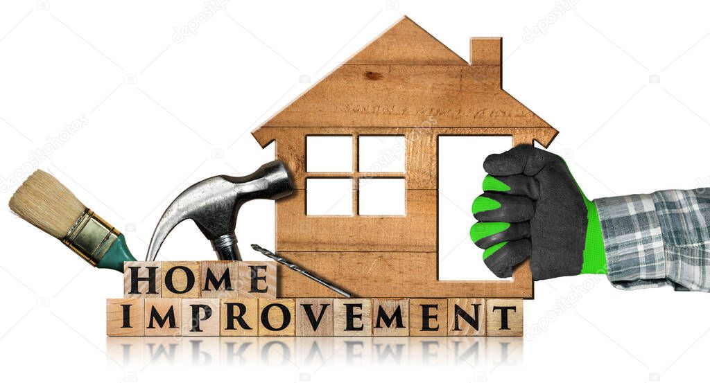 Hand with work glove holding a wooden model house with text Home Improvement made of wooden blocks, paintbrush, hammer and drill bit. Isolated on a white background.