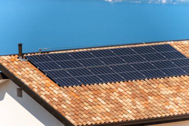 Arka planda mavi bir göl olan bir evin çatısındaki güneş panelleri. Yenilenebilir enerji kavramı