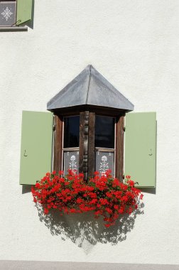 Ahşap pencereli ve kırmızı sardunyalı eski ve küçük balkon, Zuoz köyü, Engadin vadisi, Graubunden kantonu, Maloja bölgesi, İsviçre, Avrupa turizm beldesi