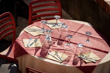 Kırmızı masa örtüsü, çatal bıçak takımı, bardaklar ve kağıt peçeteli bir açık hava restoranı masası. Yukarıdan bak, Liguria, İtalya, Avrupa