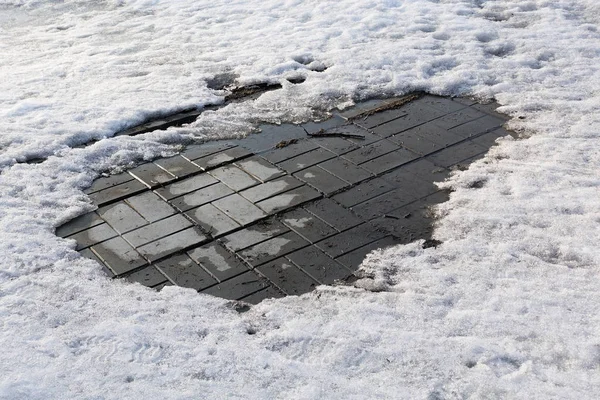 Closeup photograph of melting snow on a pavement made of gray concrete tiles. — Stock Photo, Image