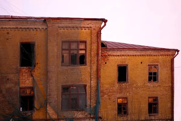 Prázdná zničená budova se zlomeným okny. Růžové nebe Sunset. Fotografie v červených barvách. Represivní atmosféra zkázy. Scenérie hororových filmů — Stock fotografie