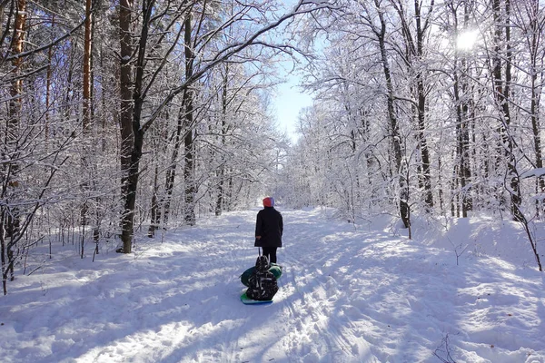 Mamma rullar sin lilla son på slangen i parken på vintern. Lycklig familj utomhus. vinter roligt för små barn. — Stockfoto