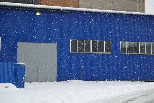 Snowfall on the background of an industrial warehouse of blue me — Stock Photo, Image