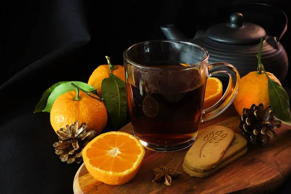 Thé d'automne. Une tasse de thé noir, une cuillère, des feuilles d'automne, des mandarines. Biscuits au gingembre. Fond noir — Photo