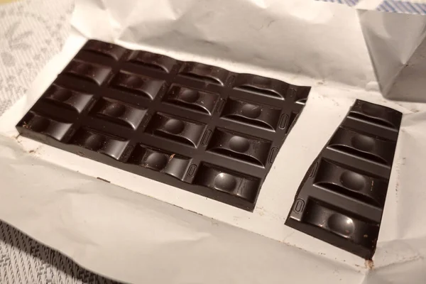 Gebroken zwarte chocoladereep op wit inpakpapier — Stockfoto