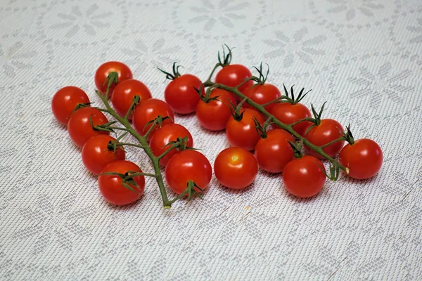 Tomates cerises sur une branche en deux rangées sur une table avec une nappe couverture — Photo