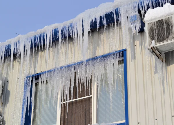 Icicles longos, grandes e perigosos em um telhado de casa de tijolo — Fotografia de Stock