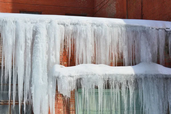 Icicles longos, grandes e perigosos em um telhado de casa de tijolo — Fotografia de Stock