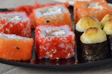 Suşi ve çubuklar ile siyah bir tabak üzerinde rulo.