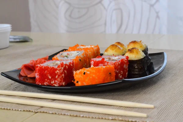 Суши и рулоны на черной тарелке с палочками для еды . — стоковое фото