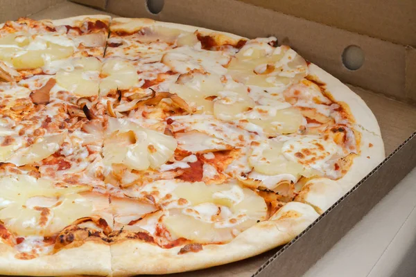 Big pineapple pizza cut into pieces in a cardboard box