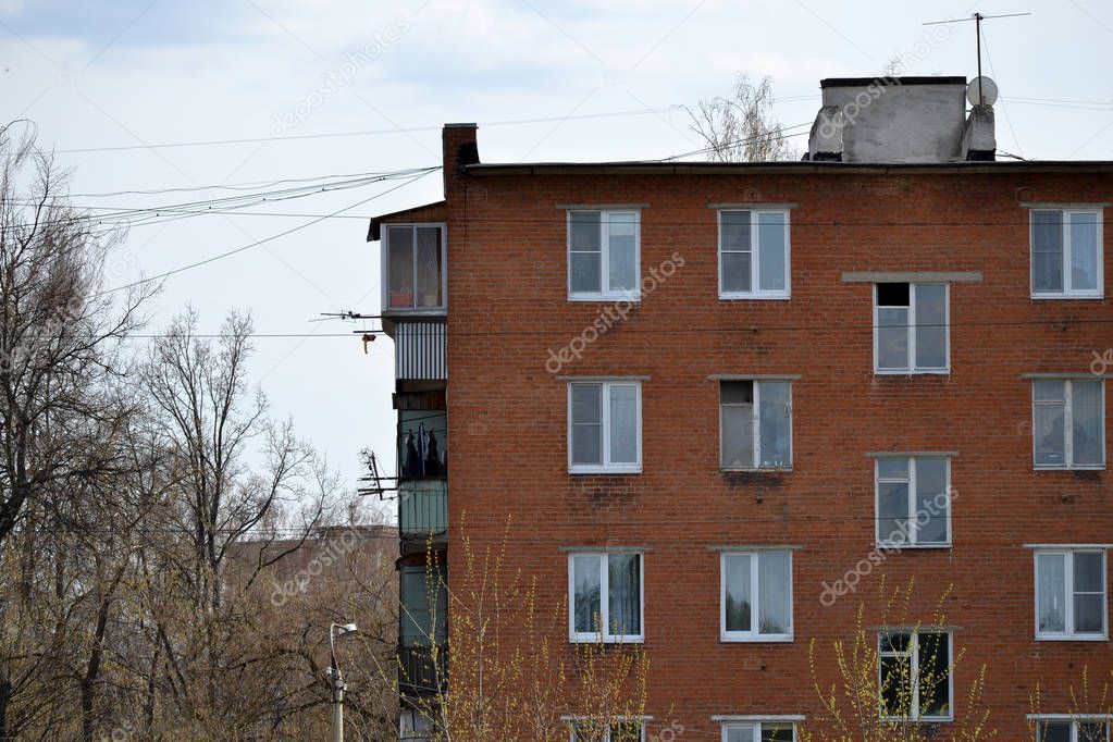 Photo of an old brick multi-storey apartment house in a poorly-developed region of Ukraine or Russia. Obsolete multi-storey building (hostel) against the background of a cloudy sky