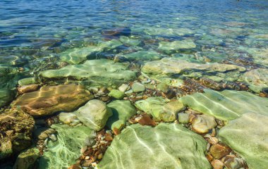 Şeffaf deniz suyu kıyıda sızıyor. Suda büyük kıyı renkli taşlar. Güzel soyut arka plan.