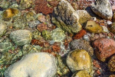 Şeffaf deniz suyu kıyıda sızıyor. Suda büyük kıyı renkli taşlar. Güzel soyut arka plan.