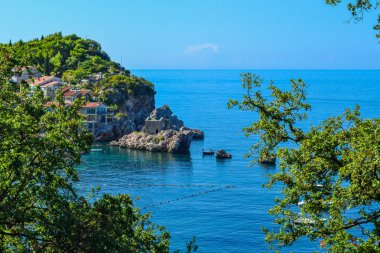 Kıyı şehri. Dağda denize yakın kiremitli çatısı olan küçük eski evler. Karadağ. Adriyatik Denizi.
