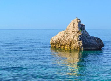 Büyük bir taş suyun üzerinde yükselir. Adriyatik Denizi. Yaz. Dalgalar olmadan sessiz deniz.