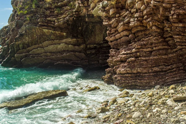 The sea view. Waves break on the stone shore. Rock and layered stone wave structure, sea foam and spray.