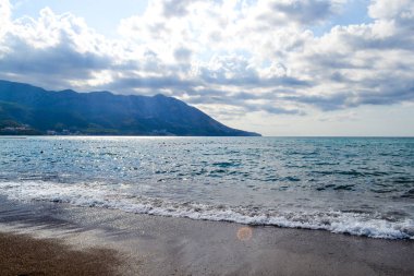 Sert havalarda deniz manzarası. Kıyıdan gelen alçak bulutlar. Yağmurlu havalarda Karadağ plajı. Karadağ'ın denizi ve dağları. Budva. Becici