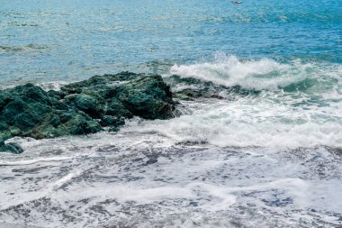Deniz dalgaları büyük yeşil bir taşa karşı kırılır..