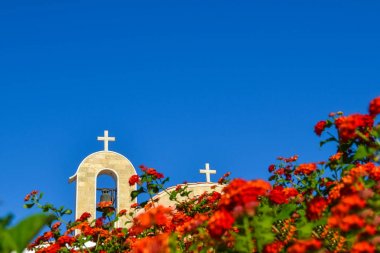 Kiremitli çatısı ve zili olan Ortodoks kilisesi. Ön planda kırmızı güller. Kıbrıs. Ayianapa mı? St. Epifani Kilisesi.