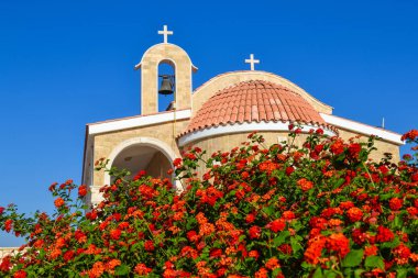 Kiremitli çatısı ve zili olan Ortodoks kilisesi. Ön planda kırmızı güller. Kıbrıs. Ayianapa mı? St. Epifani Kilisesi.