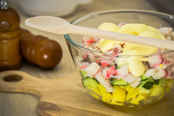 Salat aus Kartoffeln, Gurken, Krabbenstangen, Mayonnaise in einer durchsichtigen Schüssel mit einem Holzlöffel — Stockfoto