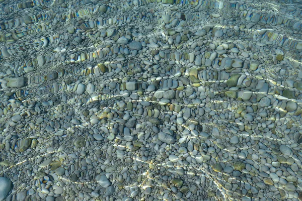 Piedras en el agua de mar y ondas. guijarros bajo el agua. Fondo náutico. Agua limpia y transparente. Mar Mediterráneo . — Foto de Stock
