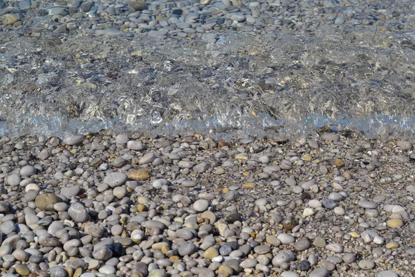 Pequenos seixos e areia molhada na praia do mar; linha de água. Calmo água transparente . — Fotografia de Stock