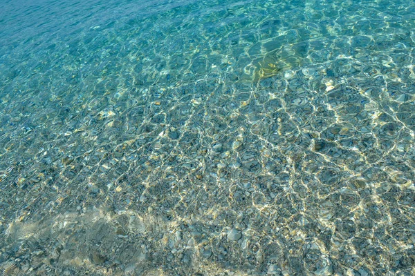 Lindos seixos coloridos e grande pedra sob água azul-turquesa clara, fundo marinho cênico ou textura, vista superior — Fotografia de Stock