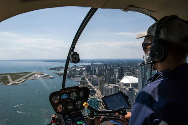 Inside view of a helicopter in flight, with man pilot. Downtown city landscape of Toronto on a sunny day.