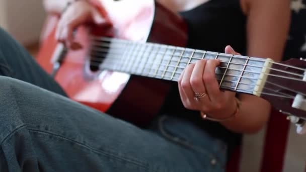 彼女の手にブレスレットを持つ若い女性がギターを弾き 文字列に触れる — ストック動画