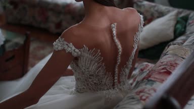 Dantel ve inciler uzun beyaz elbiseli güzel gelin odasında kanepede oturur ve elbisesinin kıvrımları düzeltiyor. 