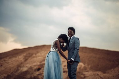 Siyah mutlu yeni evliler el ele, neşeli gülmek ve güzel manzara karşı stand.